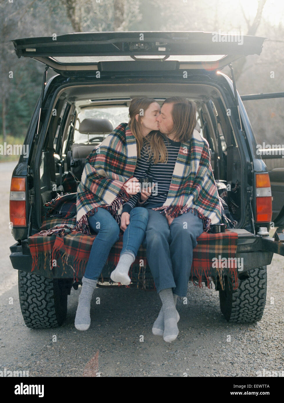 Coppia giovane seduto nella parte posteriore della loro auto, baciare. Foto Stock