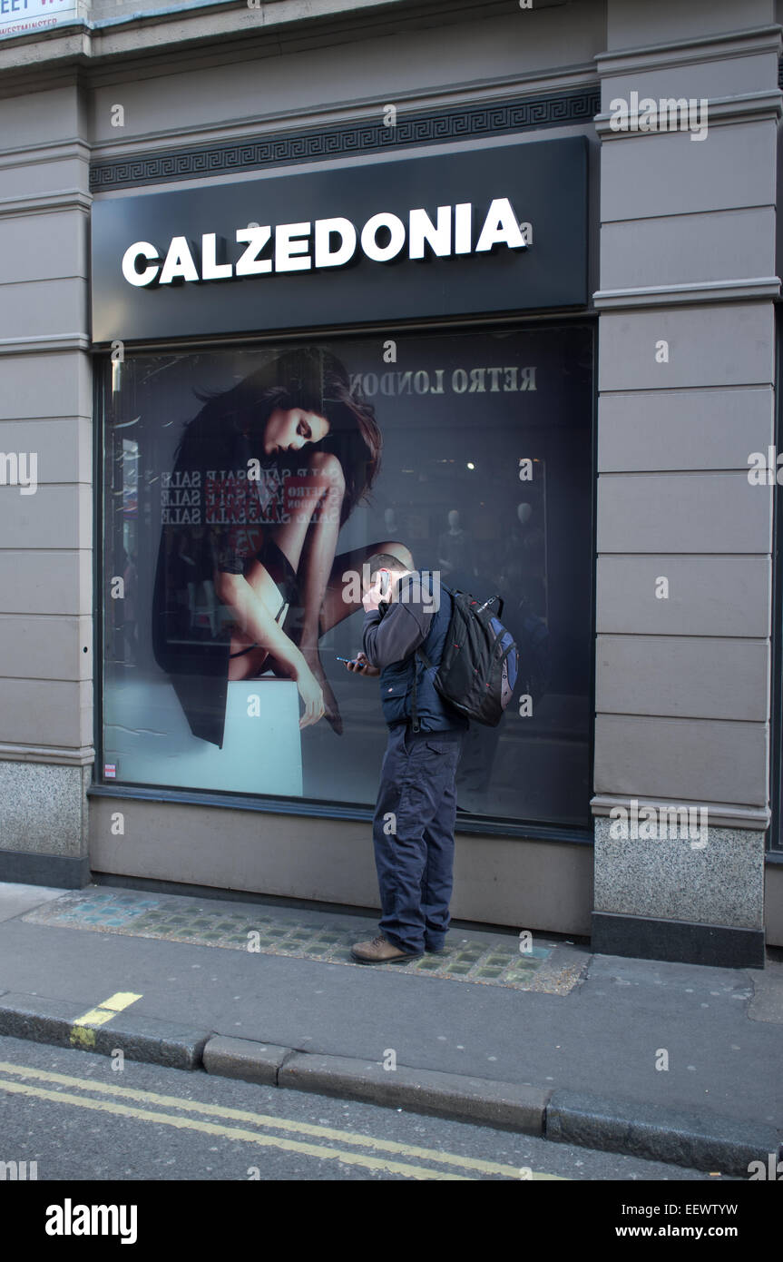 Un uomo a parlare su un telefono mobile accanto a un poster nella finestra  del negozio di abbigliamento Calzedonia Foto stock - Alamy