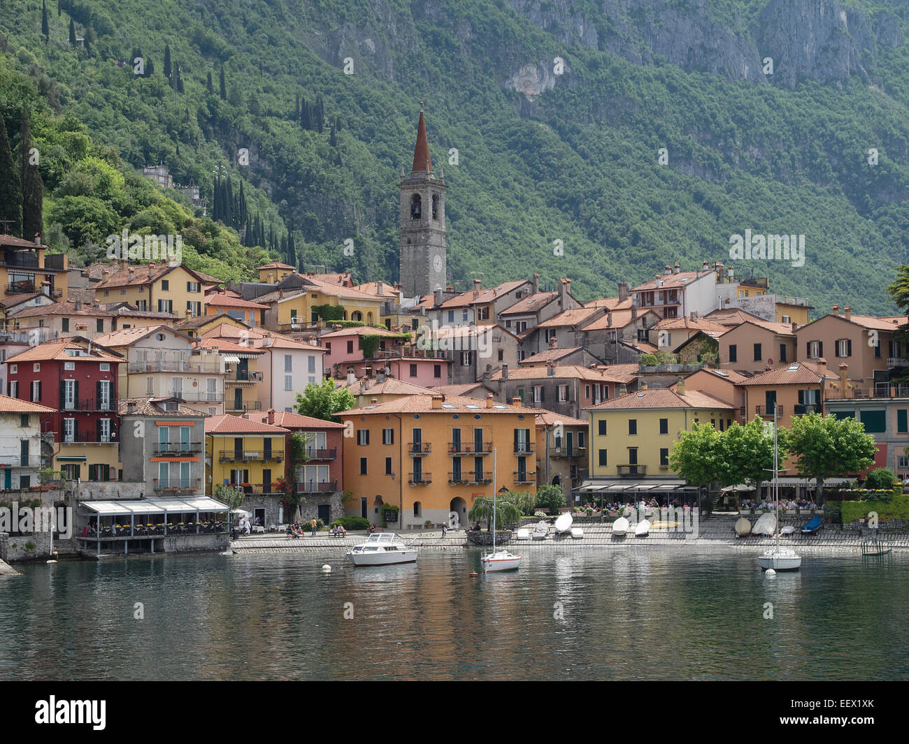 I colorati edifici sul lago e i caffè di Varenna sul Lago di Como in Italia con lo sfondo di montagne coperte di alberi Foto Stock