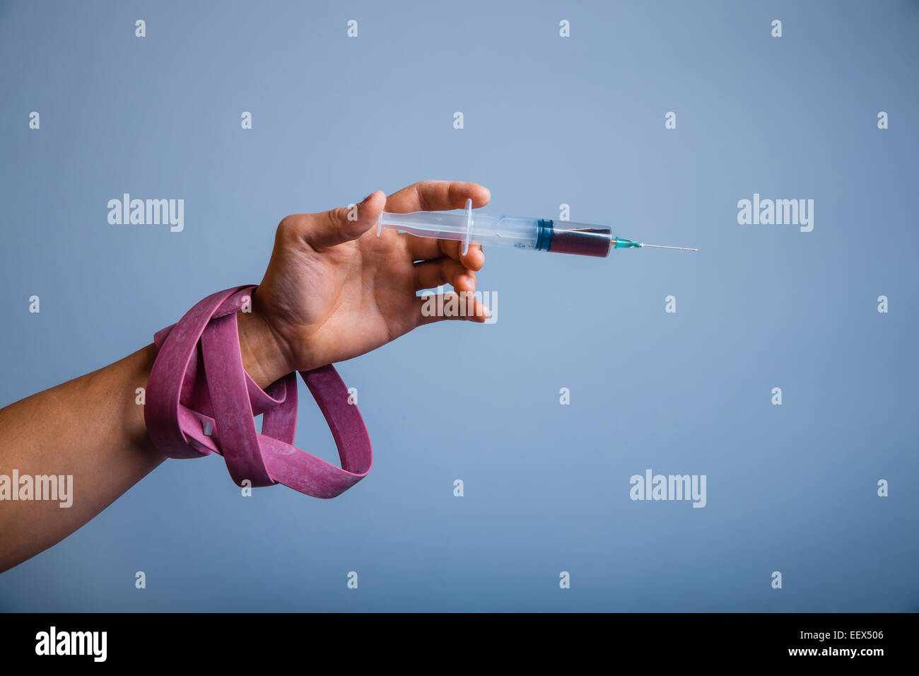 Mano con treccia tenendo la siringa il farmaco su grigio Foto Stock