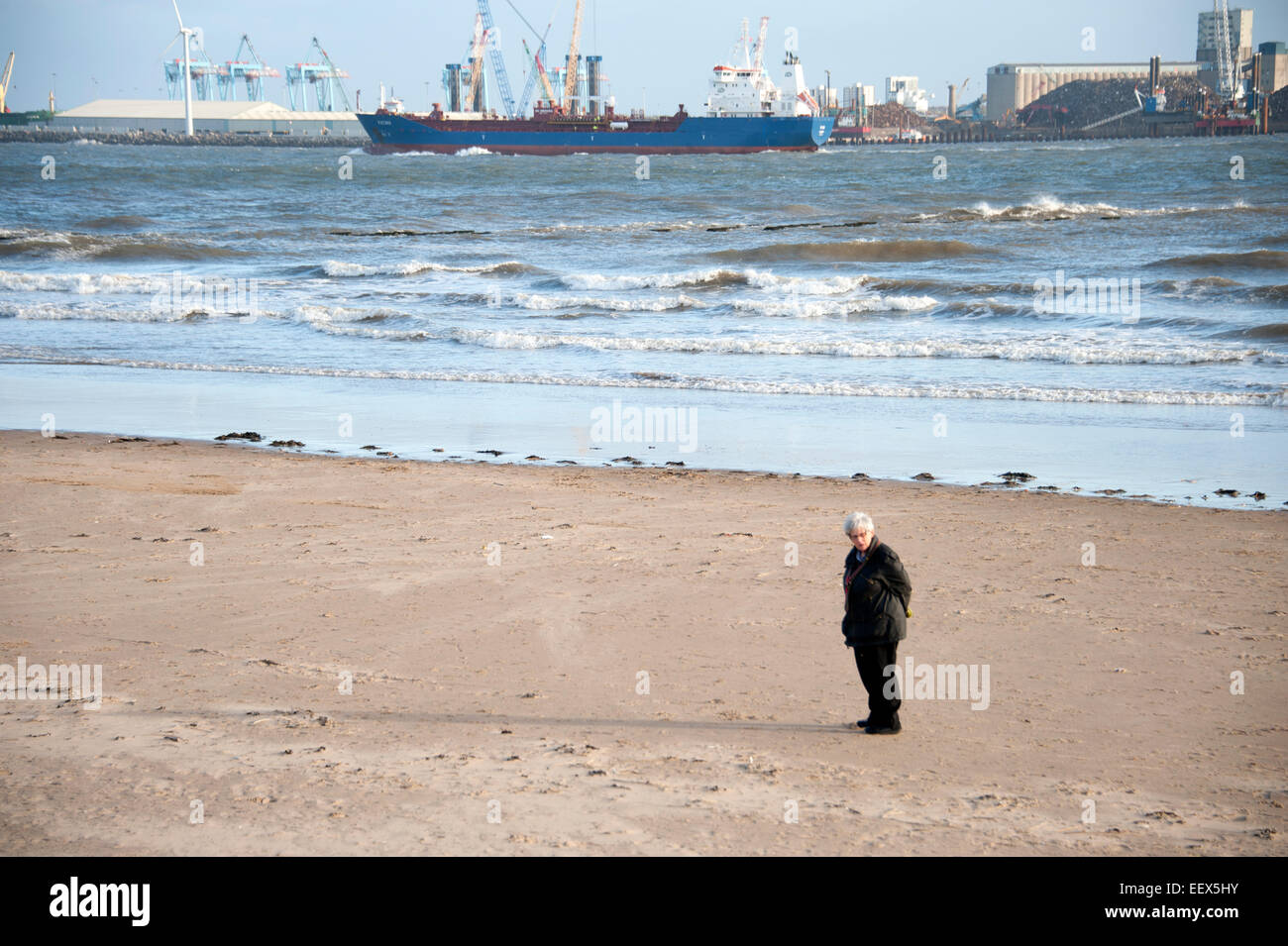 Signora anziana camminando sulla nave di spiaggia di sabbia di fiume ventoso Foto Stock