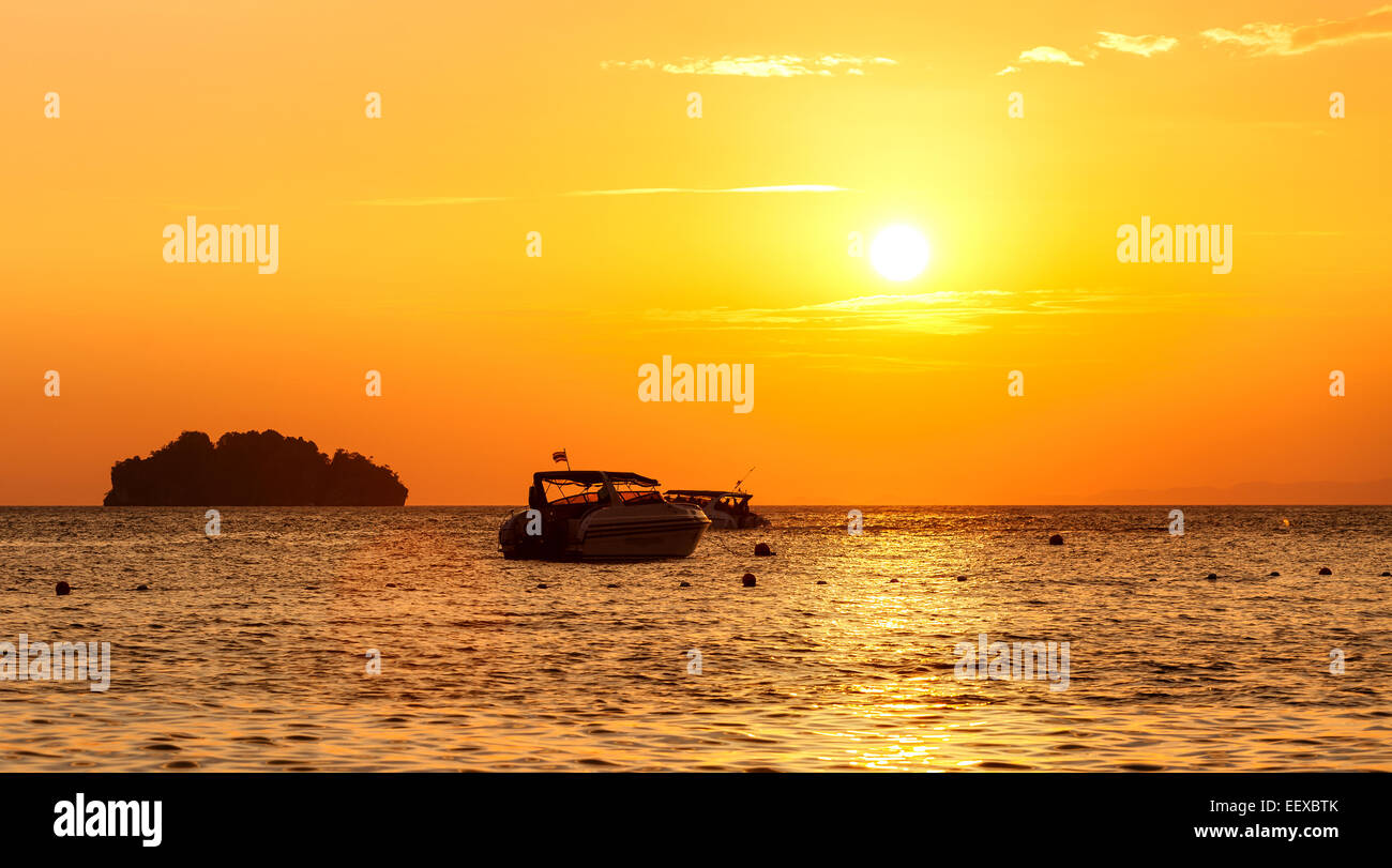 Silhouette di una piccola isola e la piccola barca al tramonto. Foto Stock