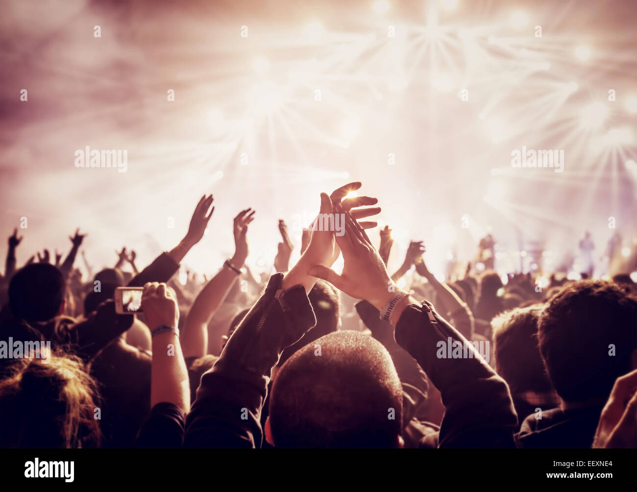 In stile vintage foto di una folla di persone felici godendo di concerto rock, sollevato in alto le mani e battendo le mani di piacere, attiva vita notturna Foto Stock