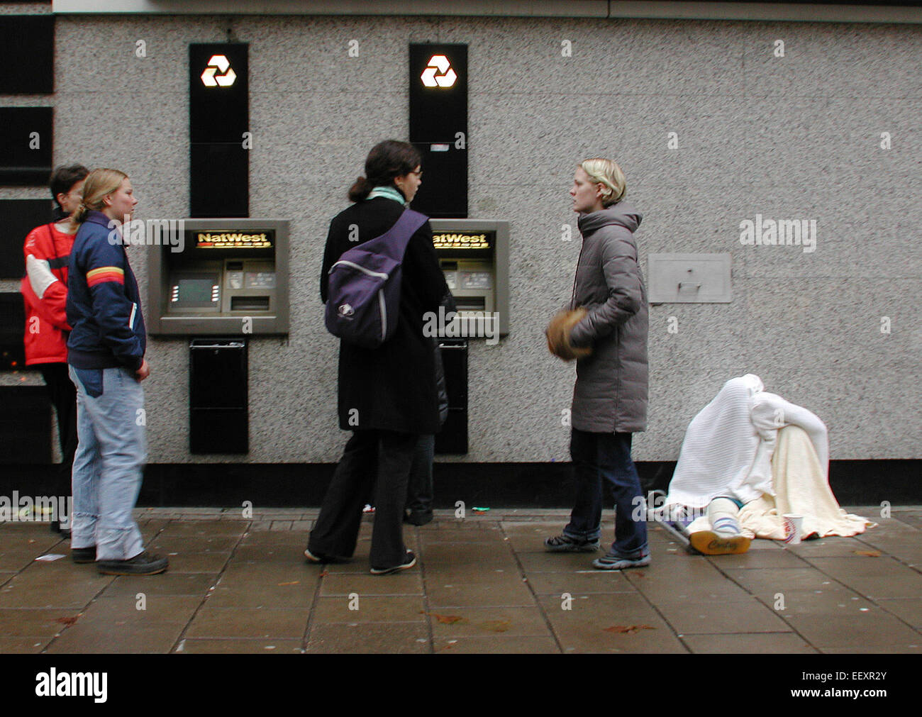 Divario ricco-povero e disuguaglianza sociale illustrato da un bancomat NatWest a Tottenham Court Road, Londra, con un disabile senza tetto coperto di coperte seduto nelle vicinanze Foto Stock