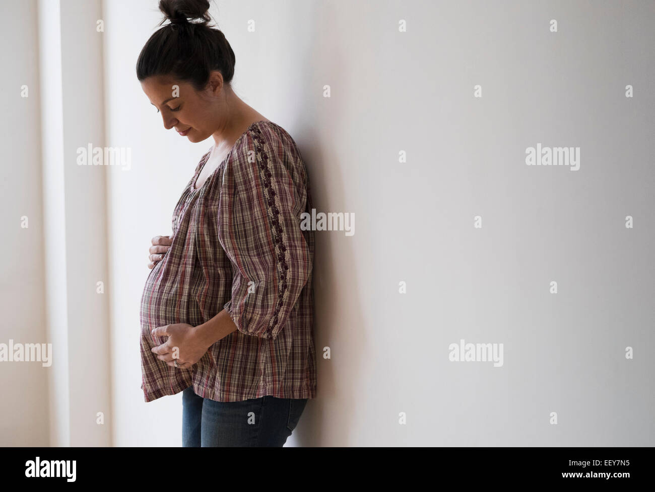 Donna incinta appoggiata contro la parete Foto Stock