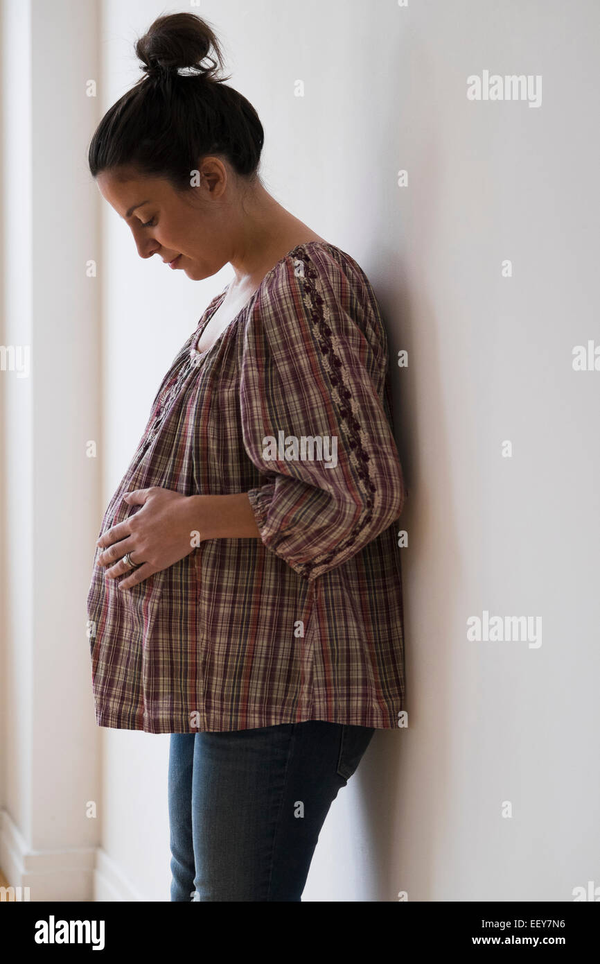 Donna incinta appoggiata contro la parete Foto Stock