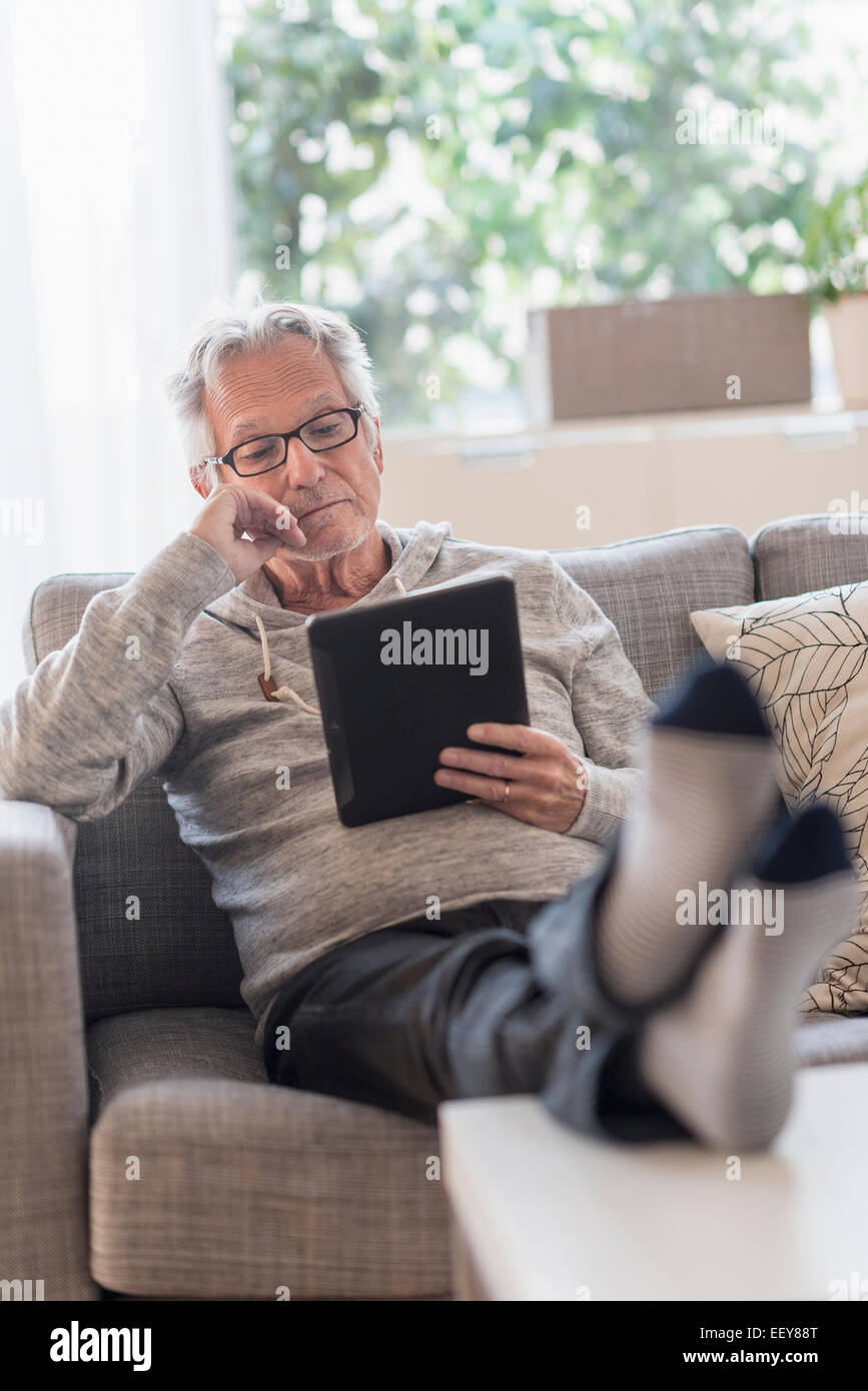 Senior uomo seduto sul divano nel soggiorno e utilizzando un tablet pc Foto Stock