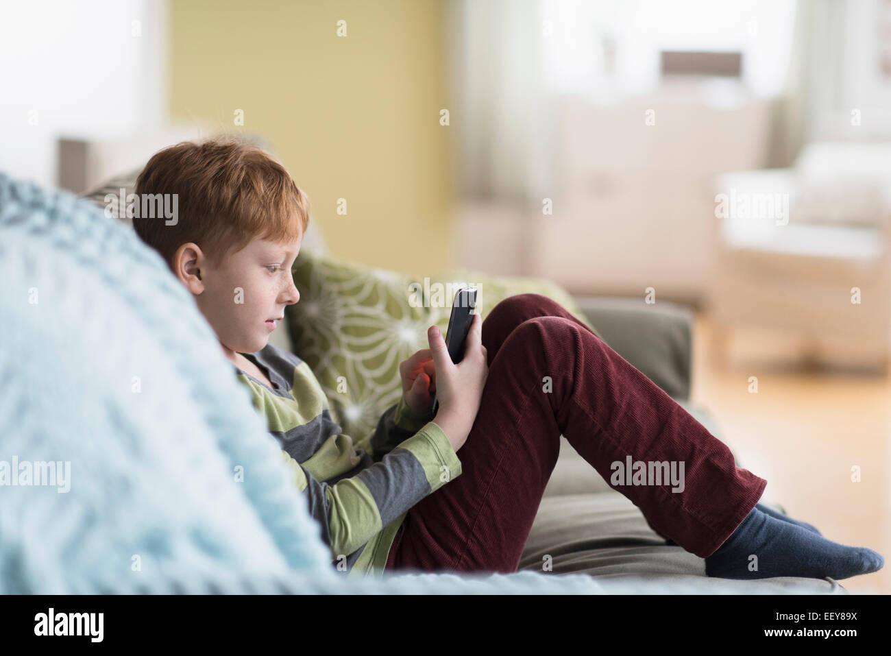 Ragazzo (6-7) seduto sul divano e utilizzando il telefono cellulare Foto Stock