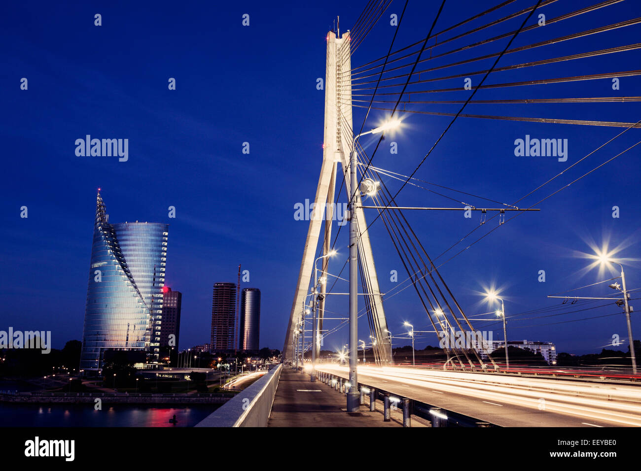 La Lettonia, Riga, ponte di sospensione con grattacieli sullo sfondo di notte Foto Stock