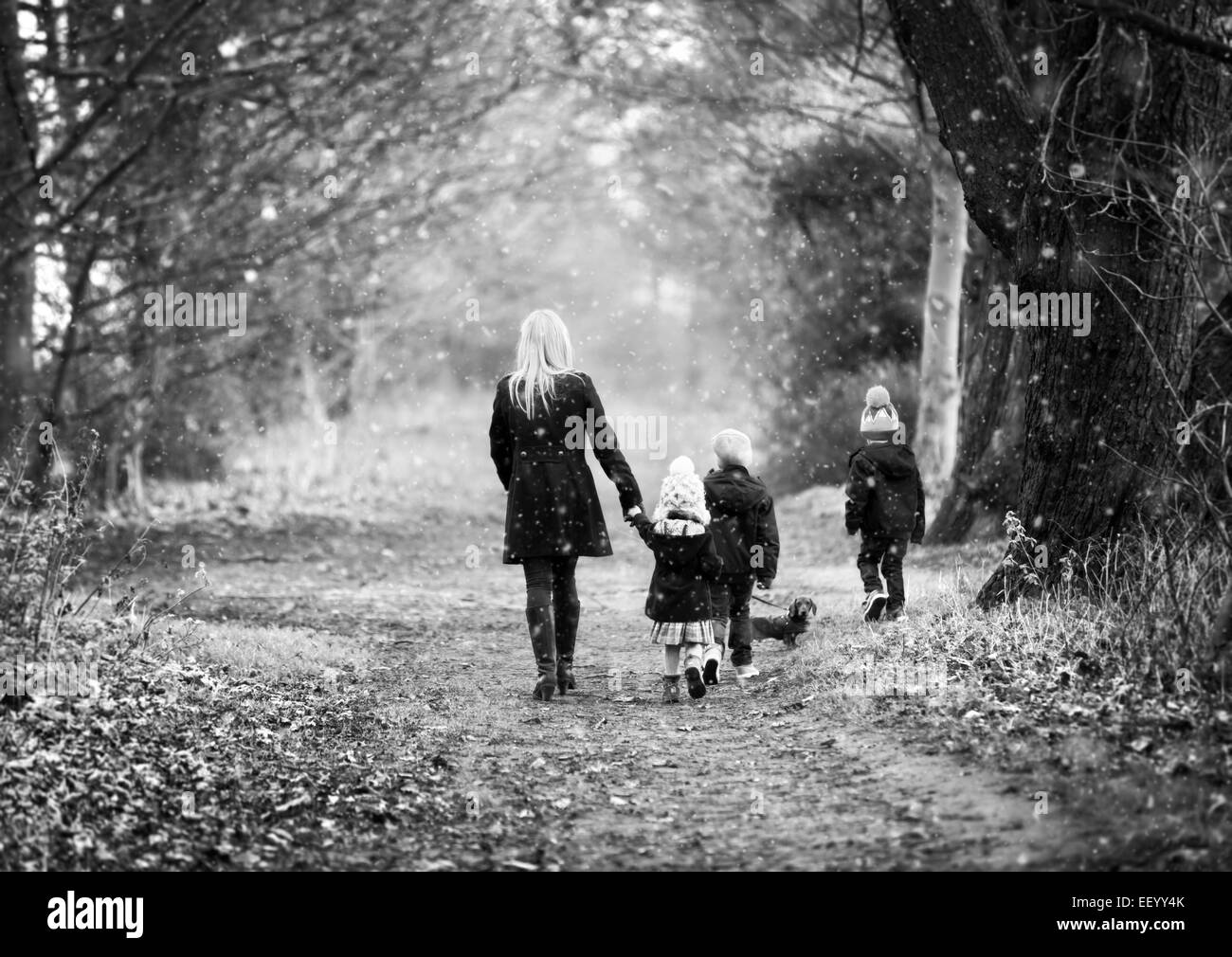 Madre e bambini sulla passeggiata invernale con il cane mentre nevicava Foto Stock