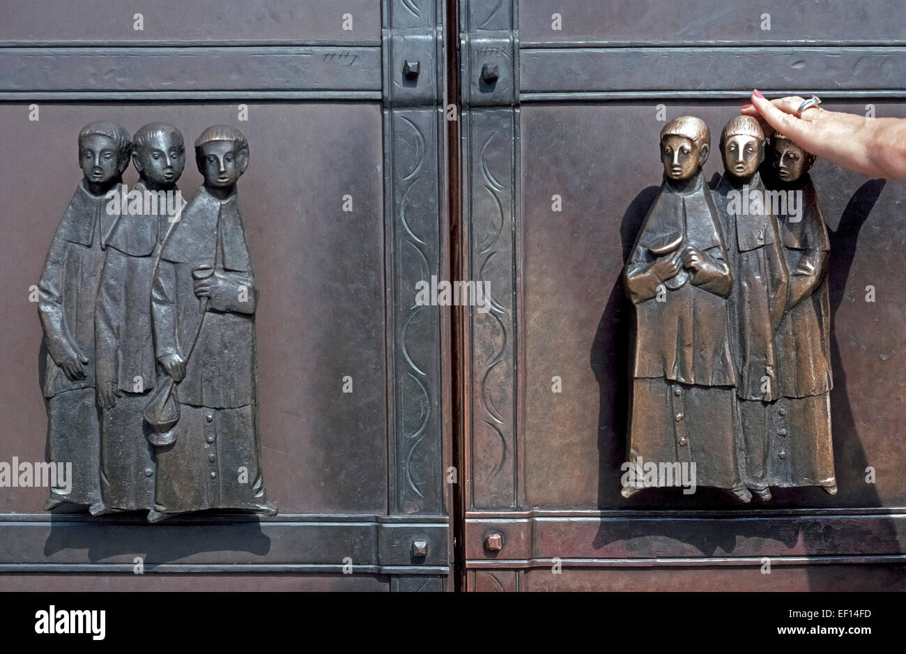 Fancy maniglie metallo forgiato con figure di solenne-di fronte i monaci nelle loro vesti sono sulle porte di ingresso di una chiesa a Berchtesgaden nelle alpi bavaresi della Germania. Gli uomini di destra sono più lucenti in aspetto poiché sono stati lucidati con le mani di adoratori che utilizzano la porta destra per entrare nella chiesa. Foto Stock