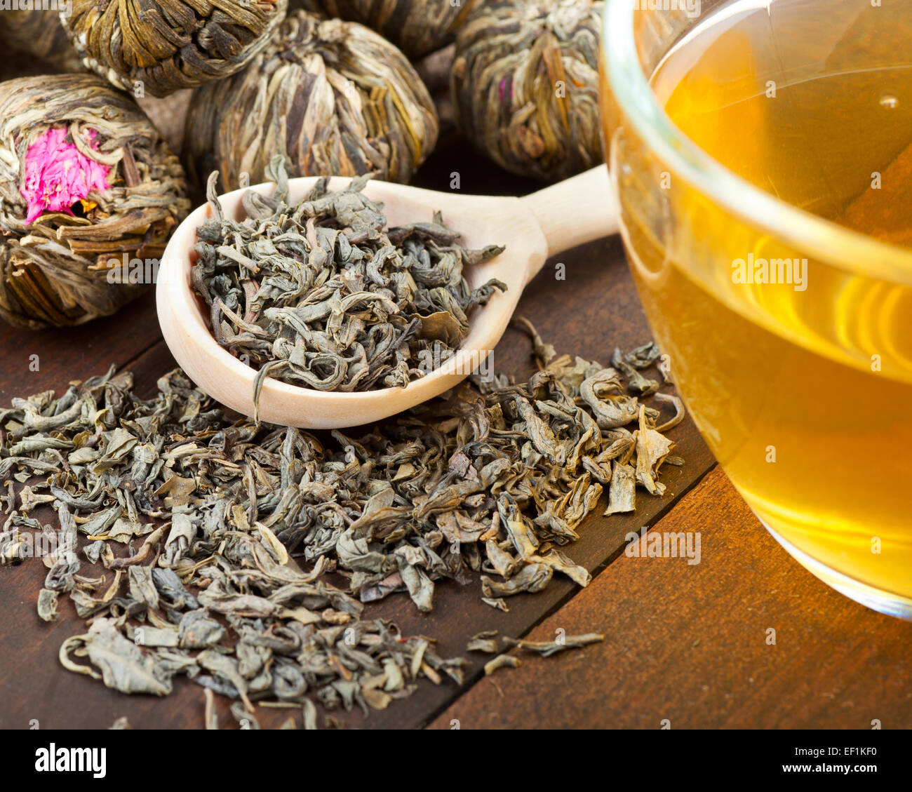 Il tè verde sfere con fiori, tazza da tè e il cucchiaio di legno sul tavolo da cucina Foto Stock