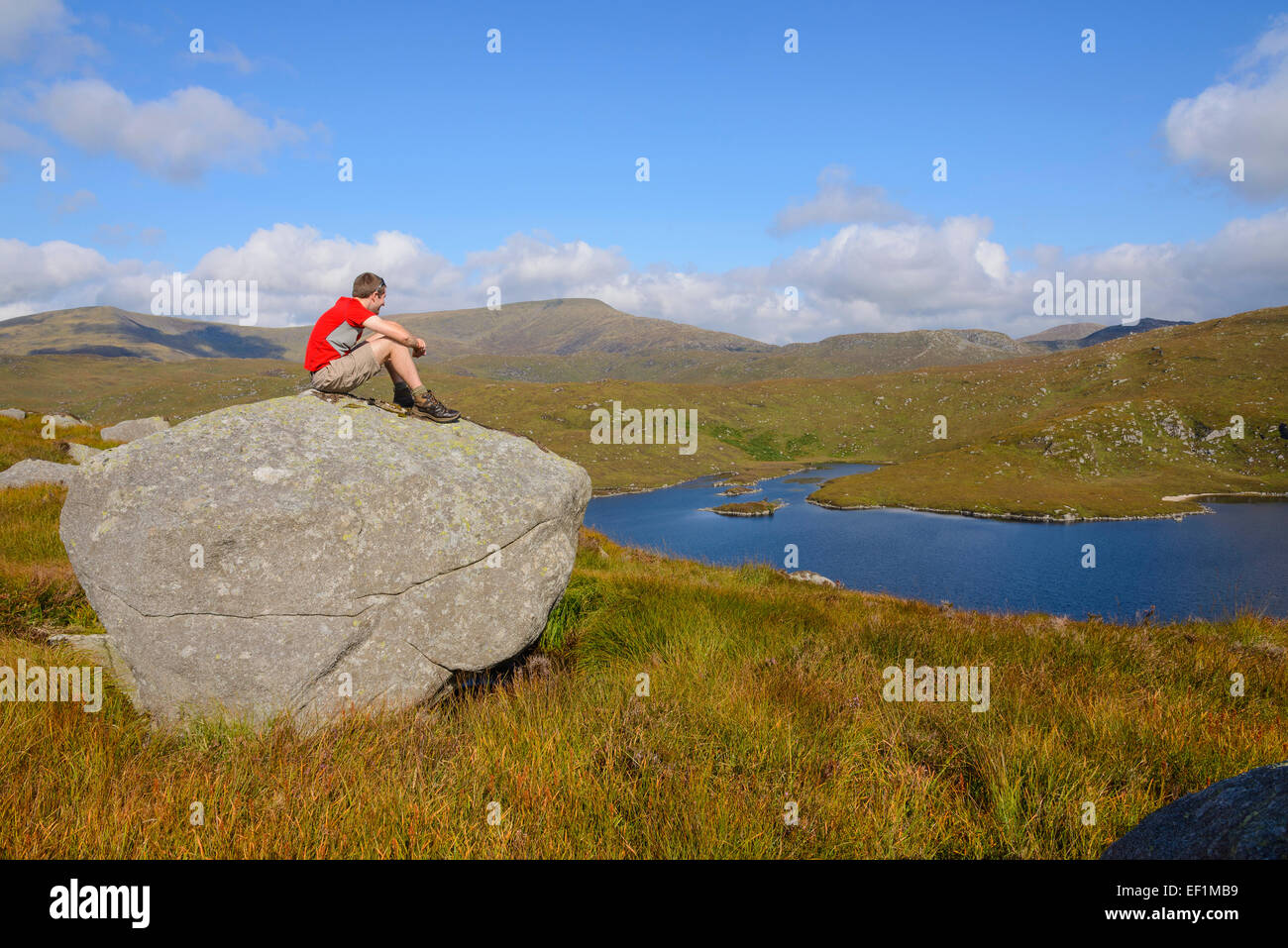 Walker seduto su una roccia, godendo della vista dal Rig del Jarkness, Galloway colline, Dumfries & Galloway, Scozia Foto Stock