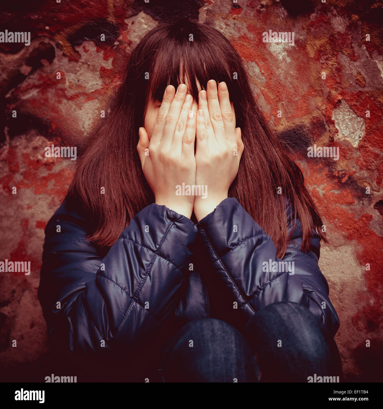 Ragazza adolescente con le mani sopra gli occhi vicino drammatica parete rossa all'aperto Foto Stock