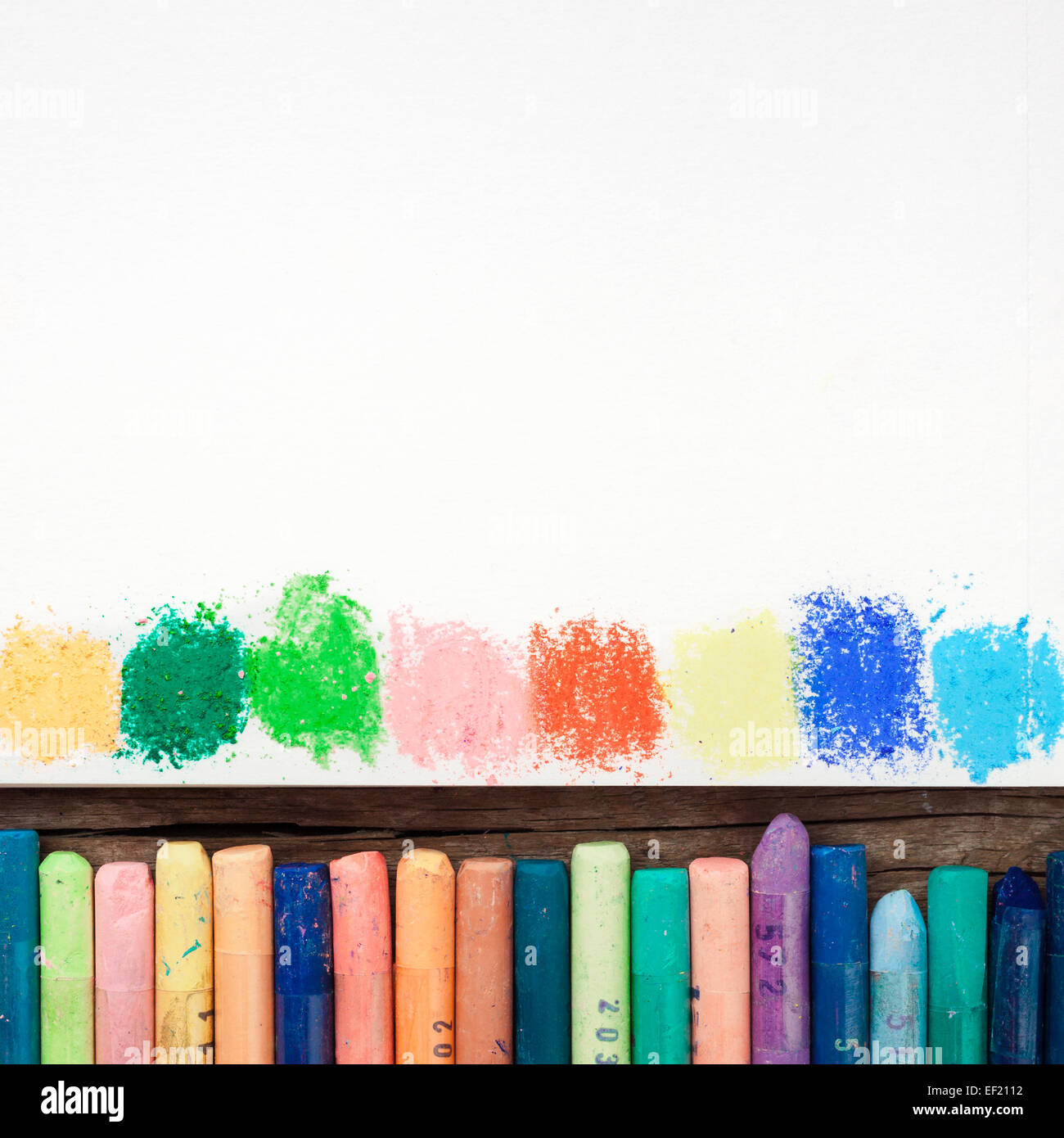 Matite di colore pastello e foglio di carta bianco di sketchbook con macchie arcobaleno di vernici. Foto Stock