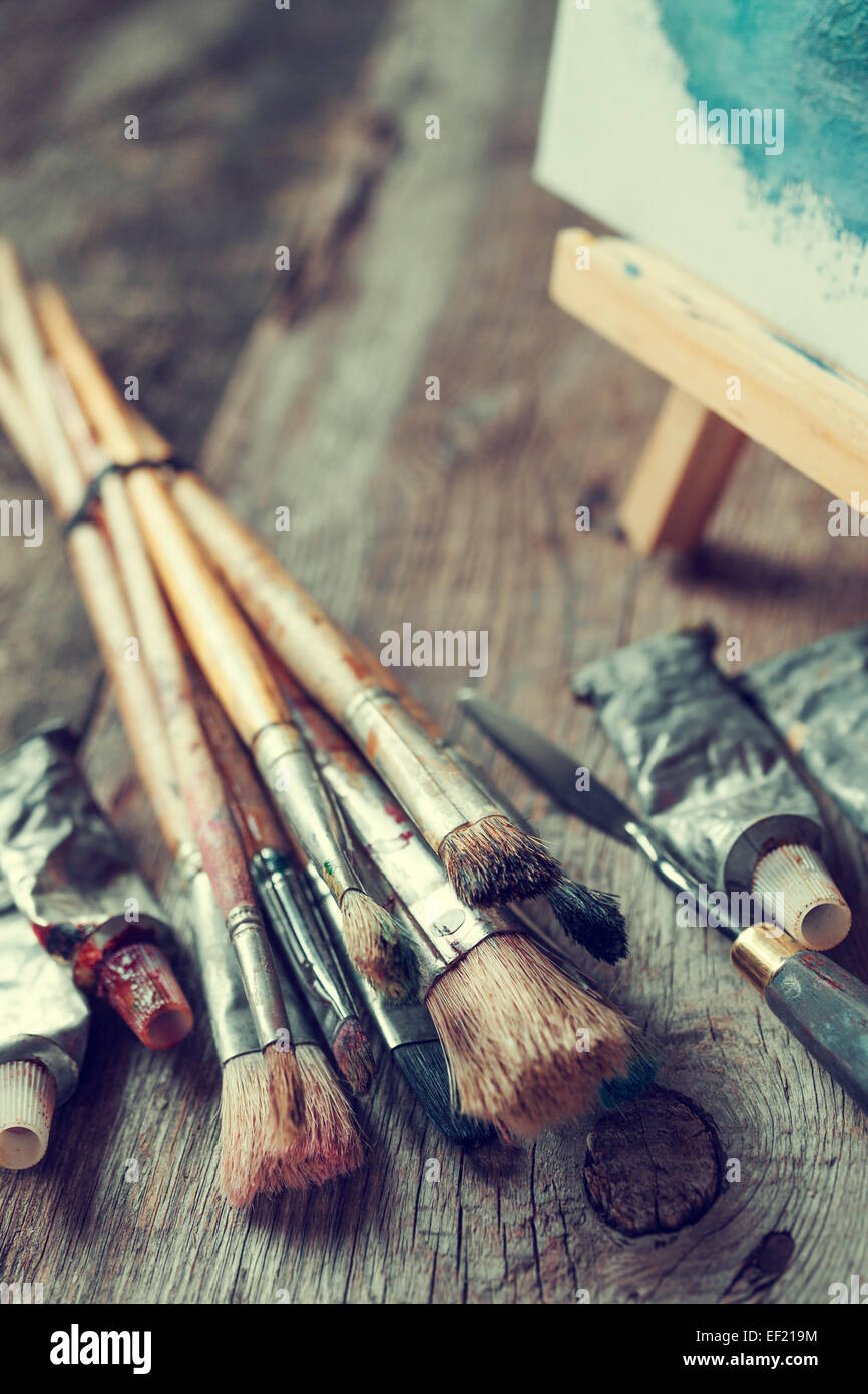 Pennelli artistici, tubi di pittura a olio, coltello tavolozza e cavalletto con la pittura di olio su una vecchia scrivania in legno. Foto Stock