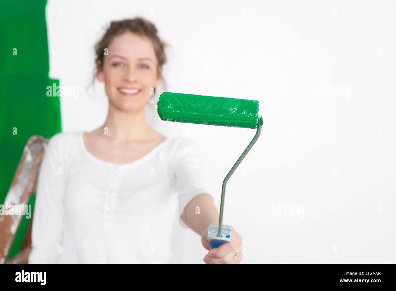 Una donna pittura un muro verde e mantiene il rullo di vernice per la fotocamera Foto Stock