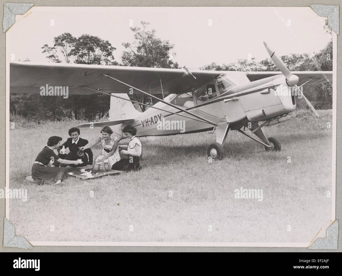 Australian donne dei piloti membro della Associazione Meg Cornwell (secondo da sinistra) e altre tre donne avente un picnic su un campo accanto a austera J/5G Cirrus Autocar monoplan VH-ready, 1954 Foto Stock