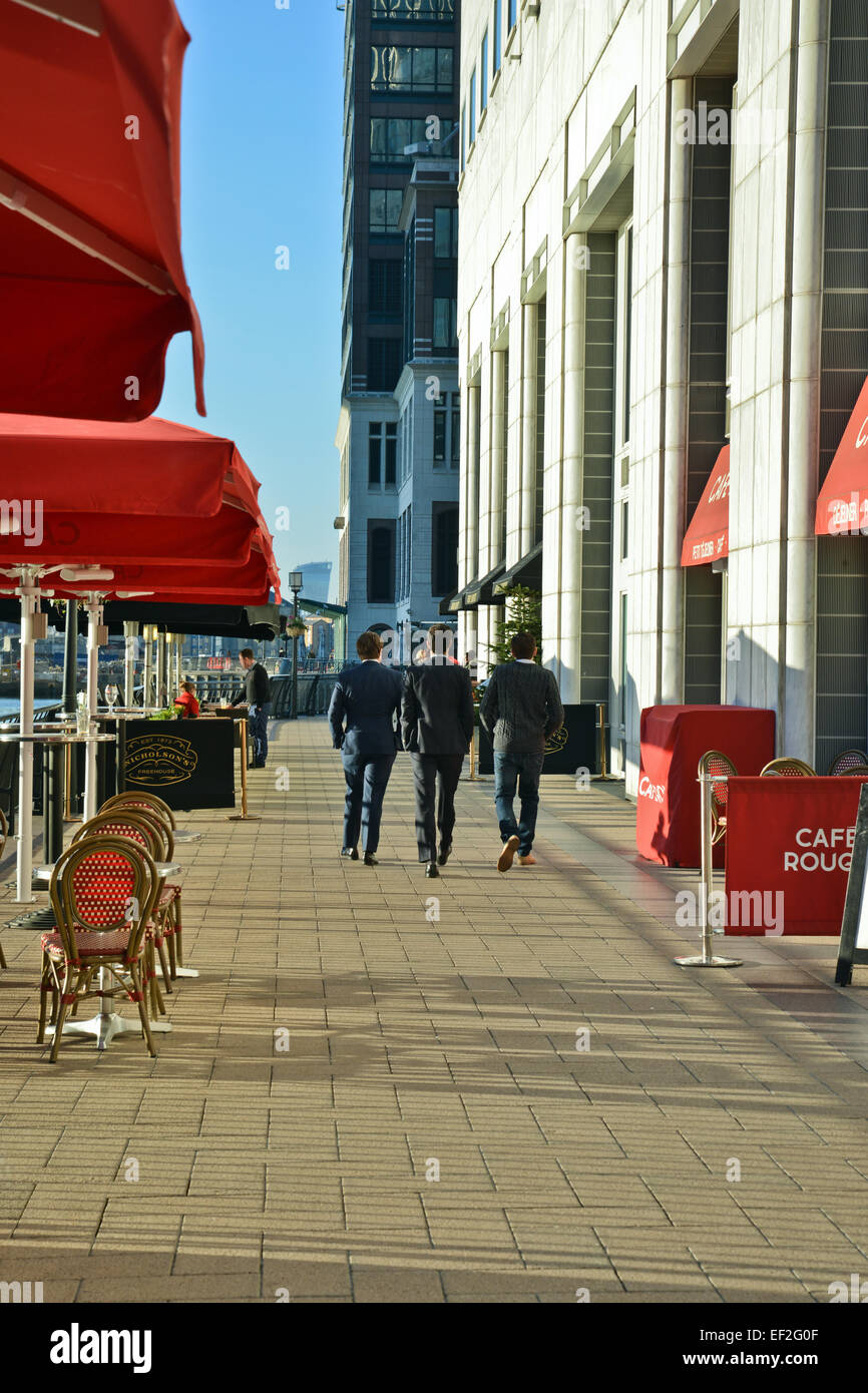 Vista posteriore di uomini di affari a piedi passato seduto fuori area caffetteria presso Canary Wharf London REGNO UNITO Foto Stock