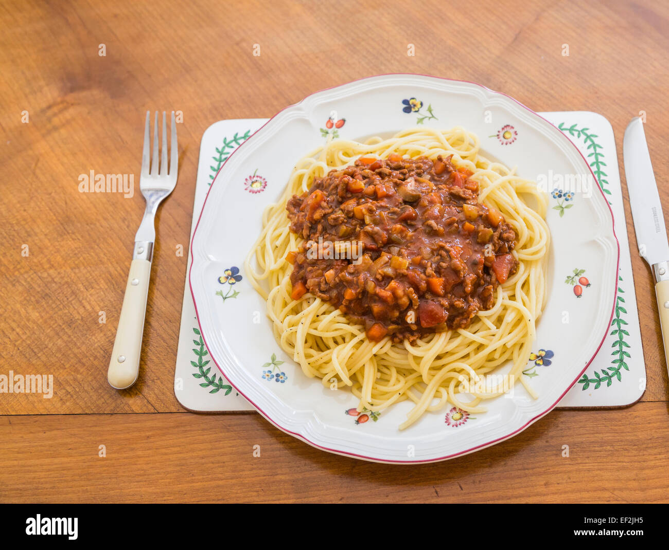 Una piastra con una grande porzione di deliziose cotte in casa spaghetti alla bolognese servita su un fiorito di porcellana bianca piastra su una tavola di legno Foto Stock