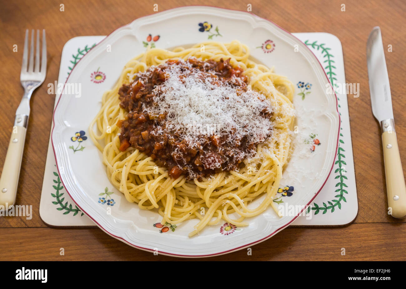 Una piastra con una grande porzione di deliziose cotte in casa spaghetti alla bolognese con formaggio parmigiano topping su un fiorito di porcellana bianca piastra su una tavola di legno Foto Stock