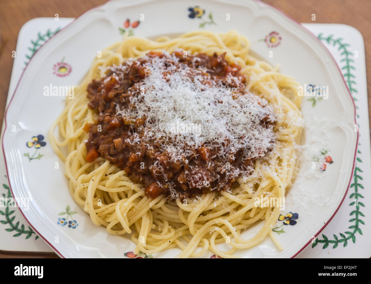 Una piastra con una grande porzione di deliziose cotte in casa spaghetti alla bolognese con formaggio parmigiano topping su un fiorito di porcellana bianca piastra su una tavola di legno Foto Stock