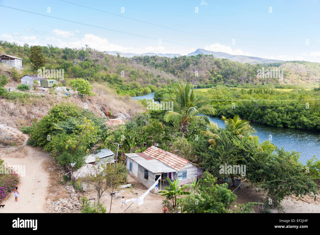 La povertà cubano lo stile di vita locale: tipica in baracche di un povero villaggio da un fiume con il lussureggiante paesaggio verde e le montagne sullo sfondo, vicino a Trinidad, Cuba Foto Stock