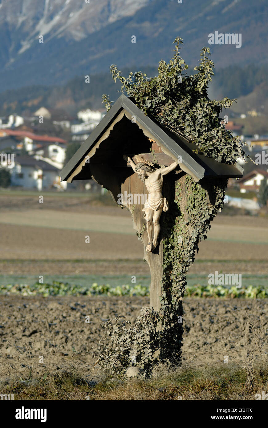 Questa immagine mostra una tradizionale "Wegkreuz" (croce a lato della strada) situata vicino a Thaur, una città in Austria. Tali croci erano storicamente collocate lungo le strade come segni religiosi, simboleggiando la protezione e la presenza divina dei viaggiatori. Foto Stock