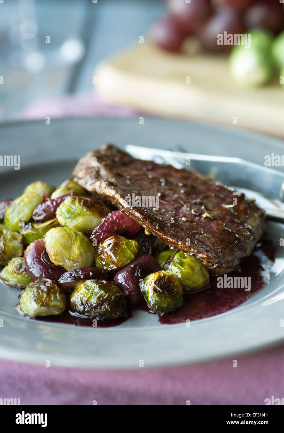 Fianchi bistecca con arrosti di cavolini di Bruxelles, uva e salsa al vino rosso Foto Stock