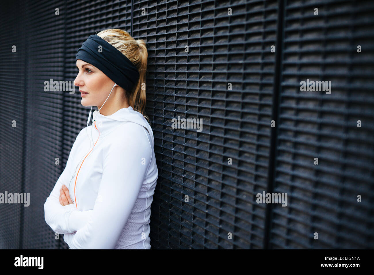 Immagine di attraente e sportivo giovane donna in piedi contro un muro che guarda lontano. Prendendo una pausa da outdoor training session. Foto Stock