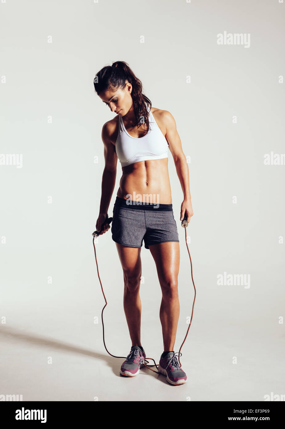 Studio shot di montare e muscolare di donna con salto con la corda in piedi su sfondo grigio. Sport e fitness concetto. Foto Stock