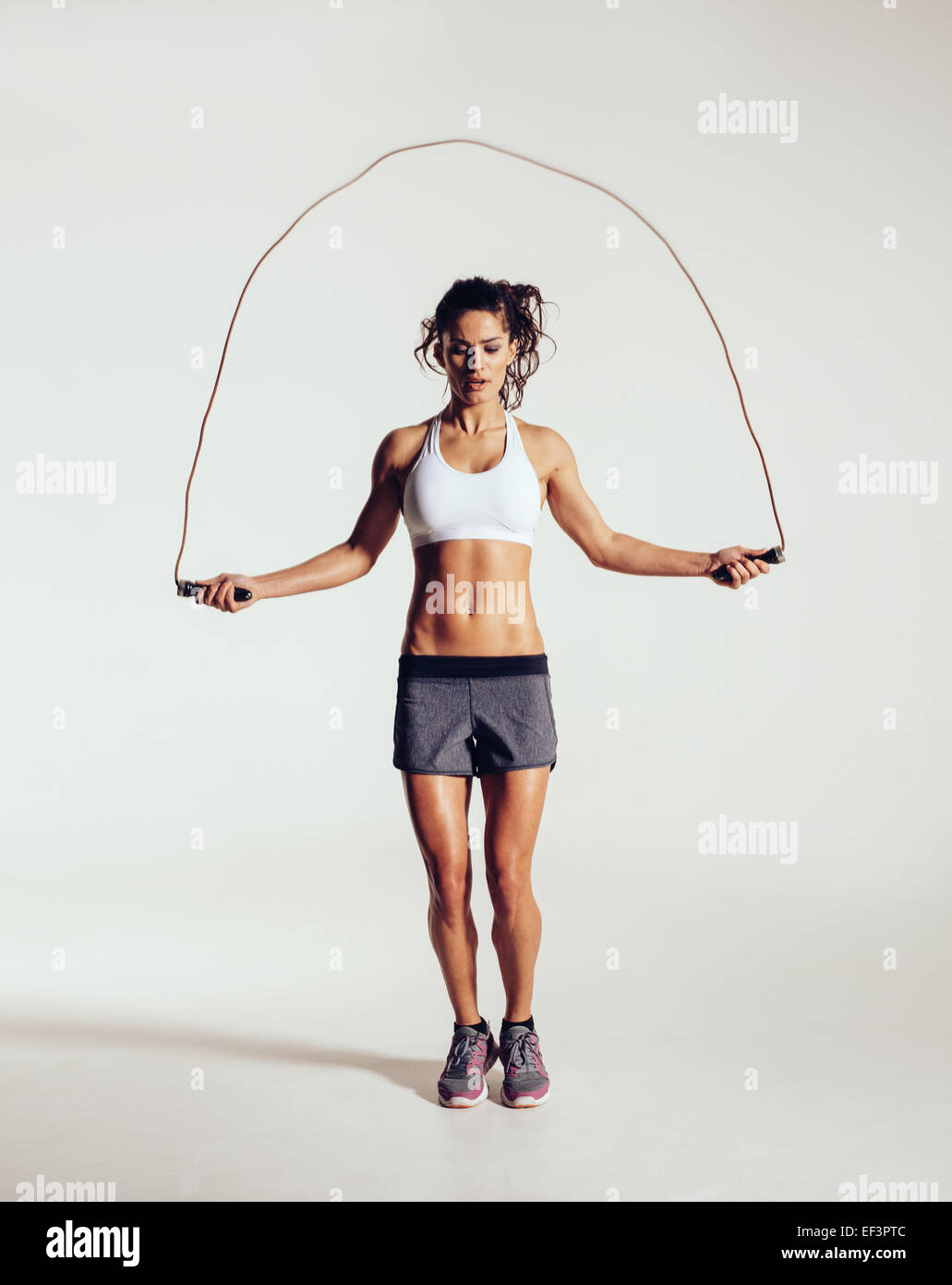Montare la giovane donna corda da salto. Ritratto di muscolare di giovane donna esercitando con salto con la corda su grigio sfondo bianco. Foto Stock