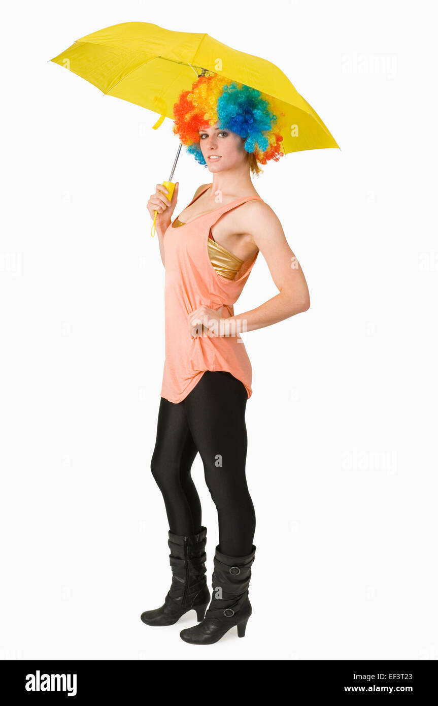 Donna che indossa un clown parrucca e azienda Ombrello giallo Foto Stock
