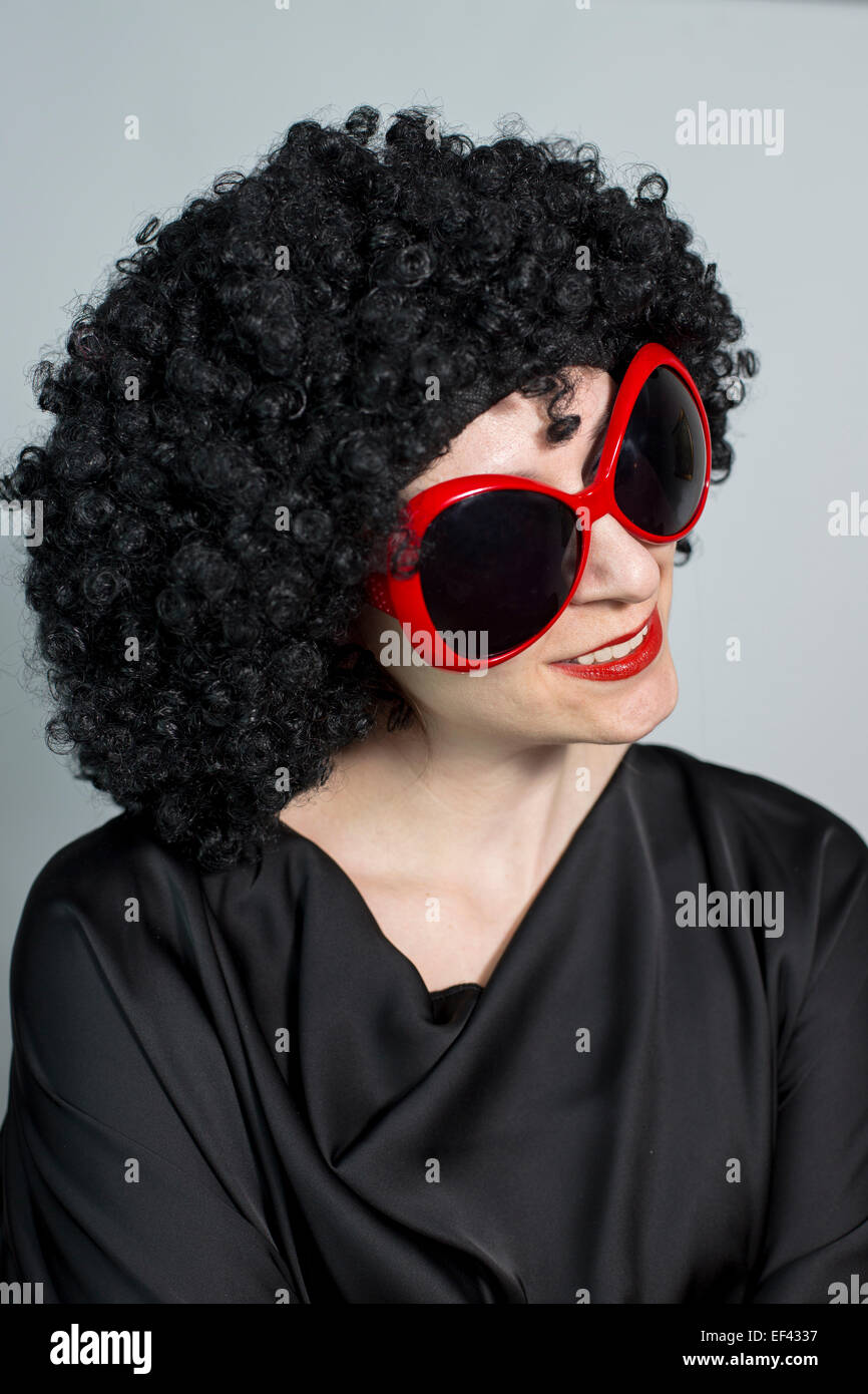 Funny red lipstic ritratto di donna che indossa una parrucca nera con occhiali rossi e posa, verticale Foto Stock