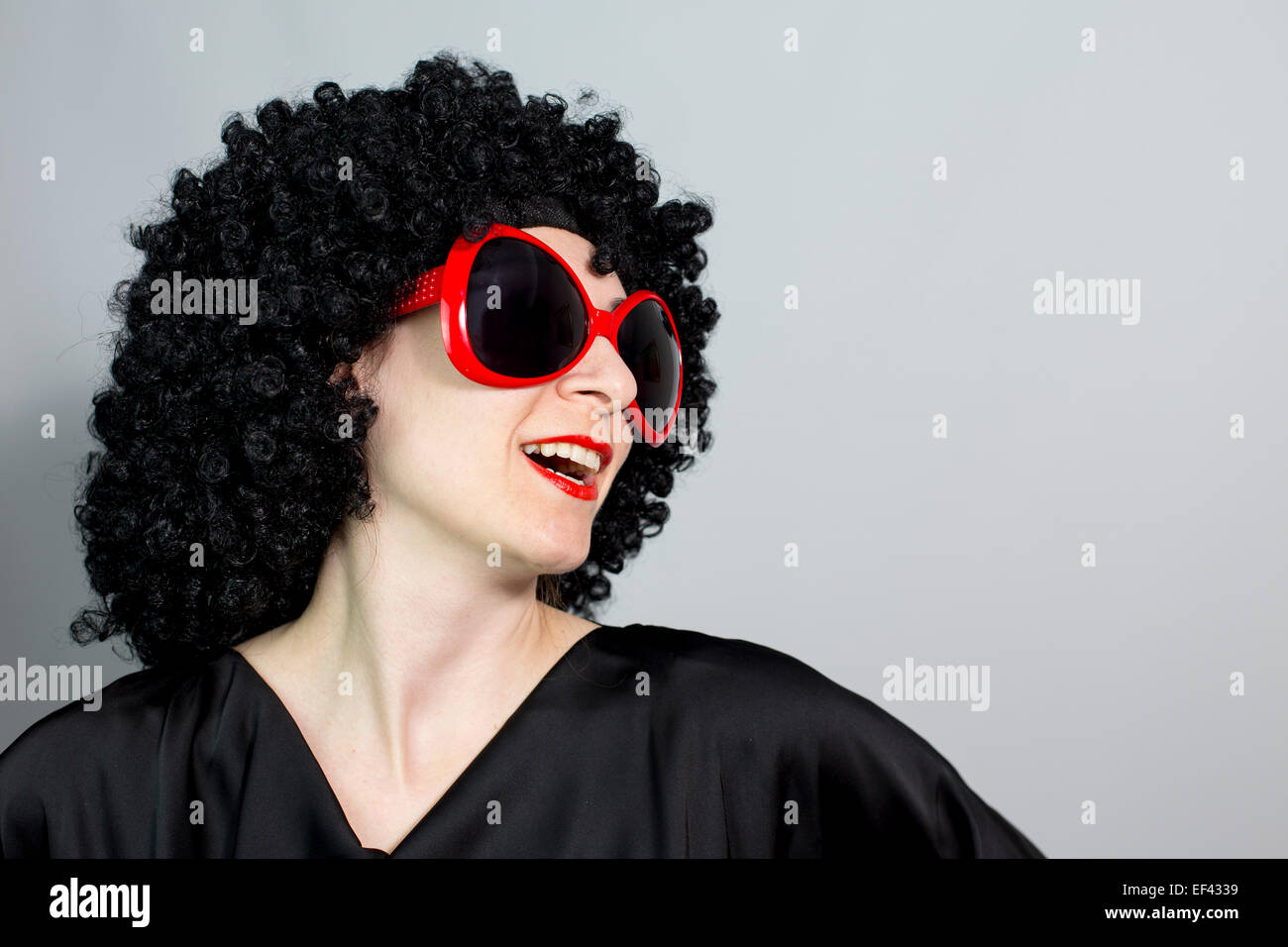 Funny red lipstic donne indossando una parrucca nera con occhiali rossi e posa, isolato di copia sullo sfondo dello spazio Foto Stock