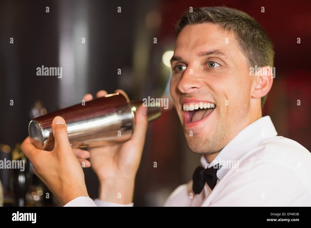 Bello il barman sorridenti in telecamera rendendo un cocktail Foto Stock