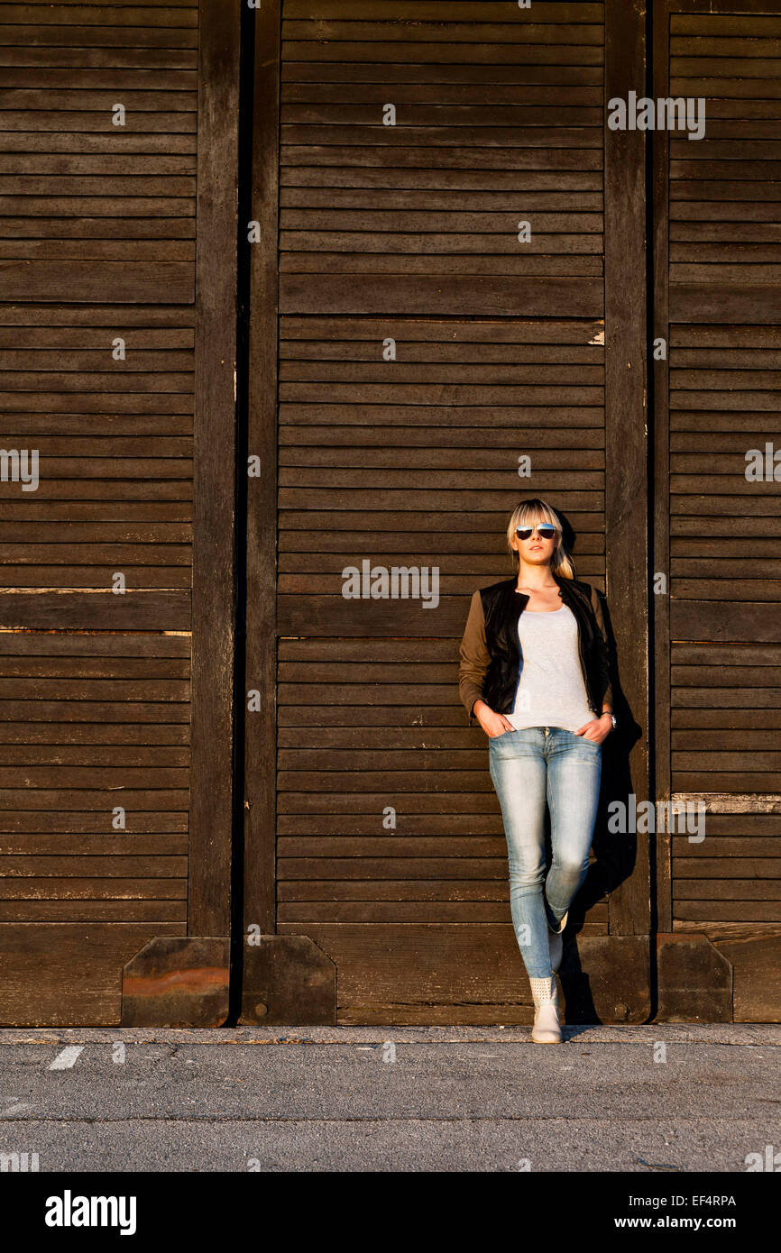 Giovane donna con occhiali da sole appoggiata contro il cancello di legno Foto Stock