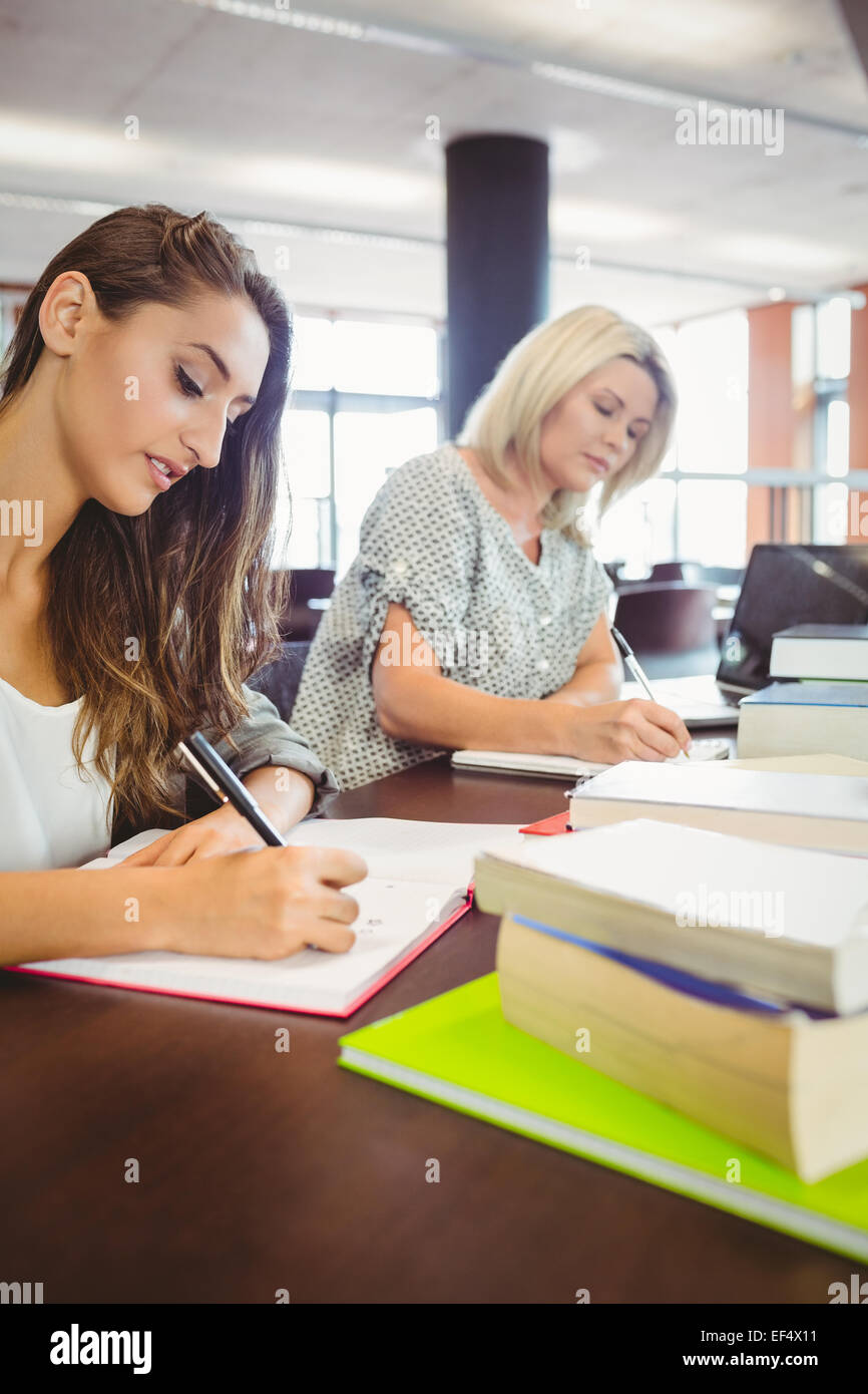Matura femmine agli studenti di scrivere le note alla scrivania Foto Stock