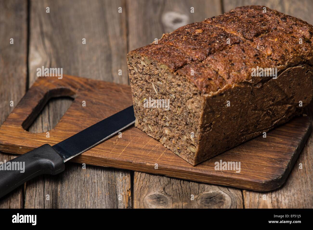 Pane integrale su breadboard di legno con coltello su sfondo di legno Foto Stock