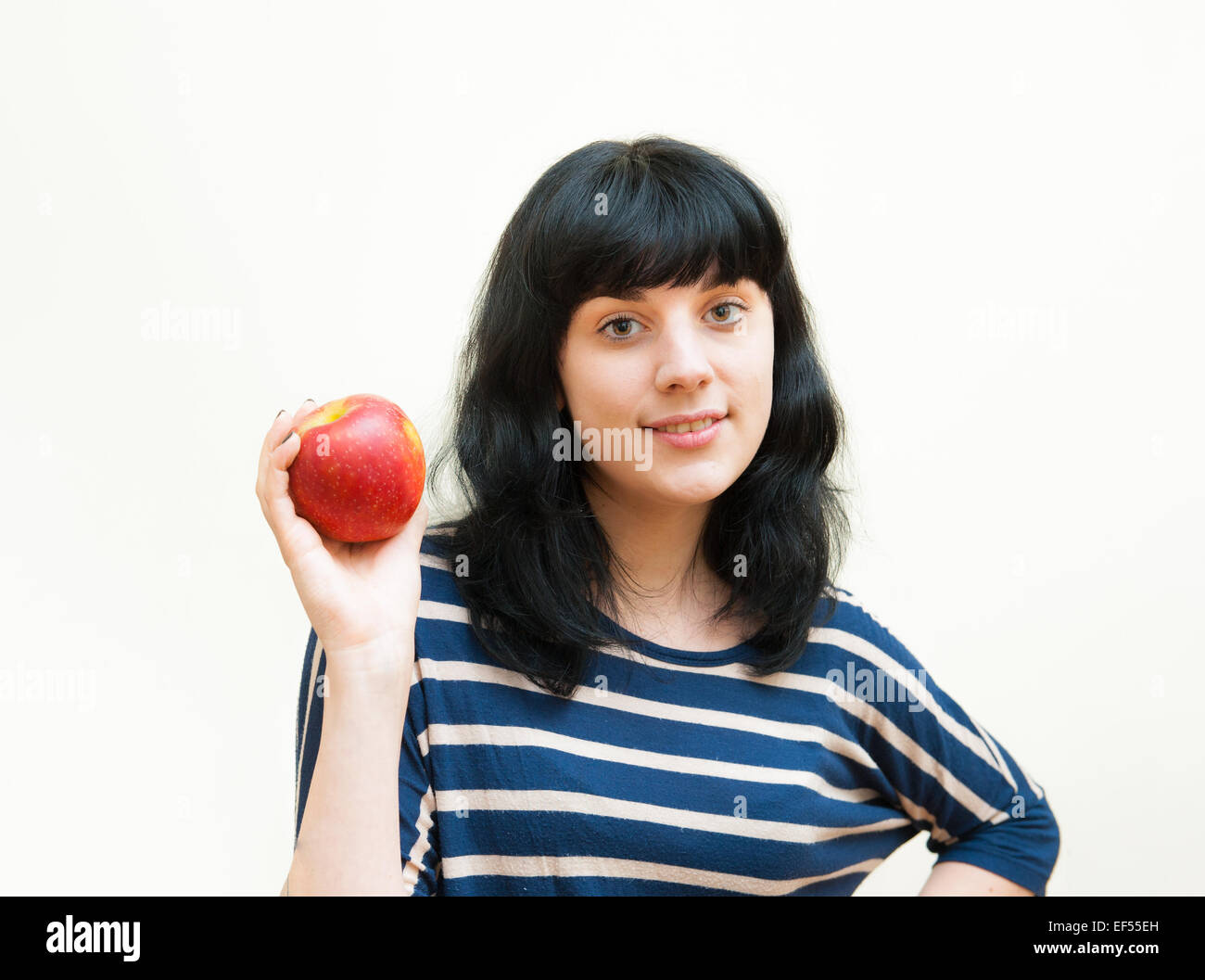 Bruna sorridente ragazza in abiti casual mostra red apple nelle sue mani su sfondo bianco Foto Stock