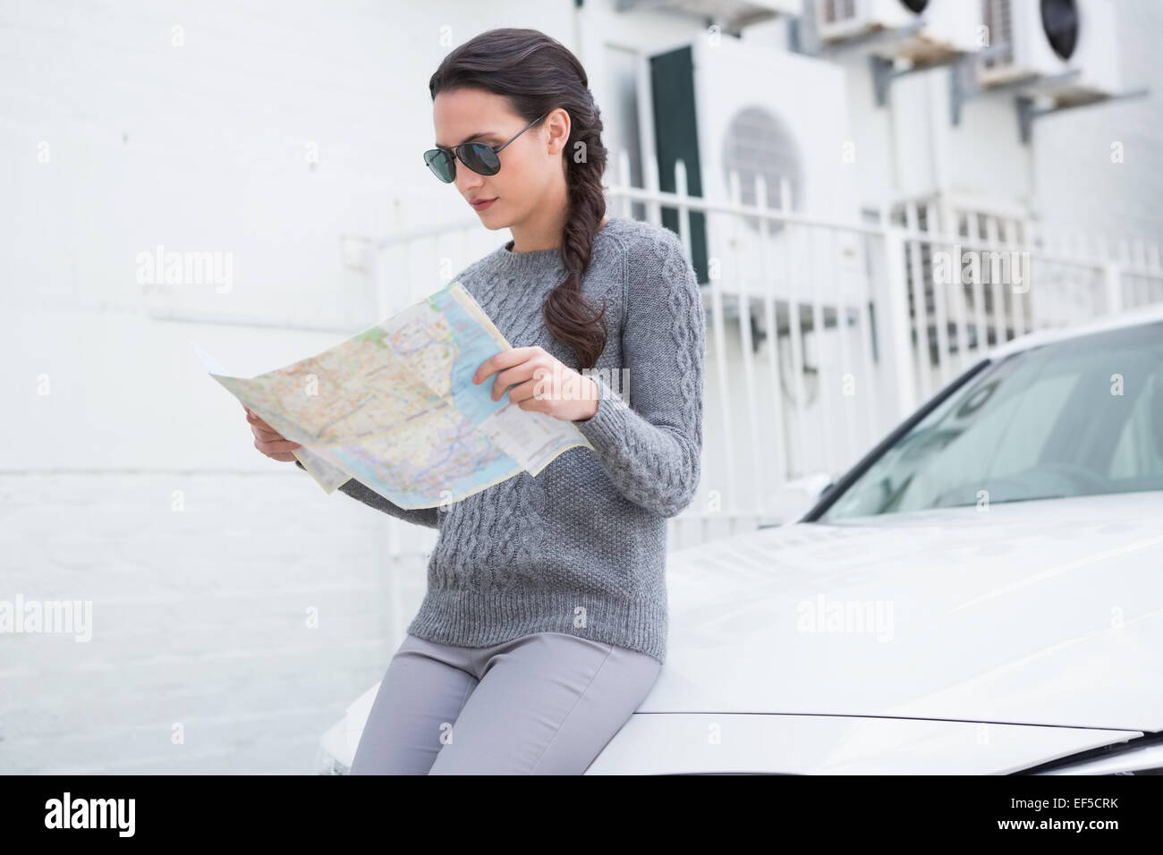 Donna che indossa gli occhiali da sole la lettura mappa accanto alla sua auto Foto Stock