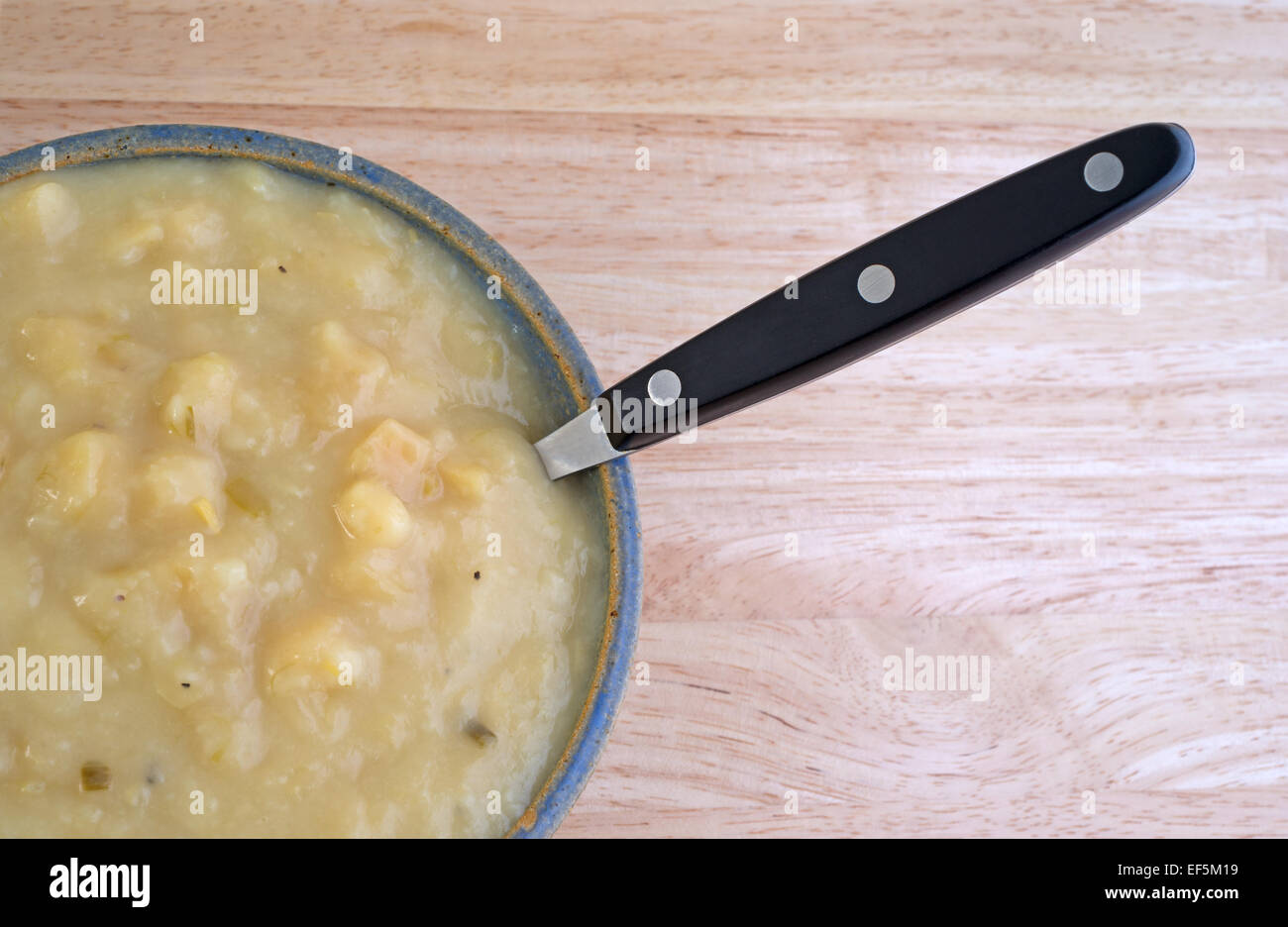 Vista parziale dall'alto di una porzione di patate e zuppa di porri in una ciotola con un cucchiaio su una tavola di legno alto. Foto Stock