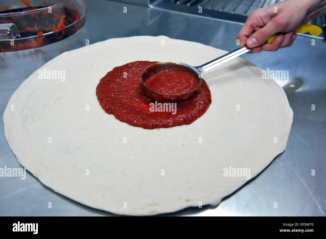 Aggiungere la salsa di pomodoro di una base per pizza in un ristorante fast food. Foto Stock