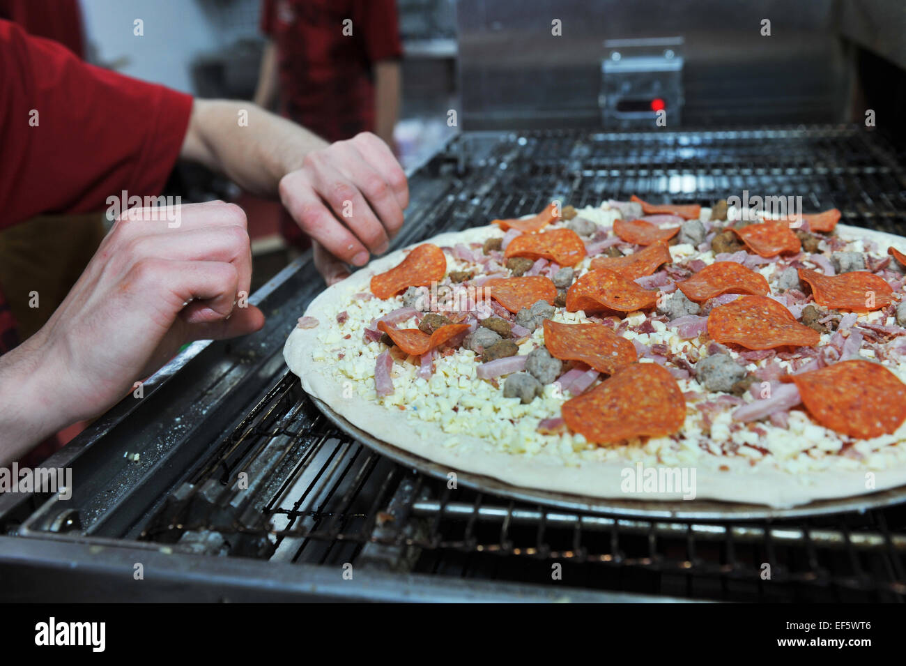 Close up rendendo le pizze in un takeaway, Leeds il caricamento della pizza nel nastro trasportatore forno. Foto Stock