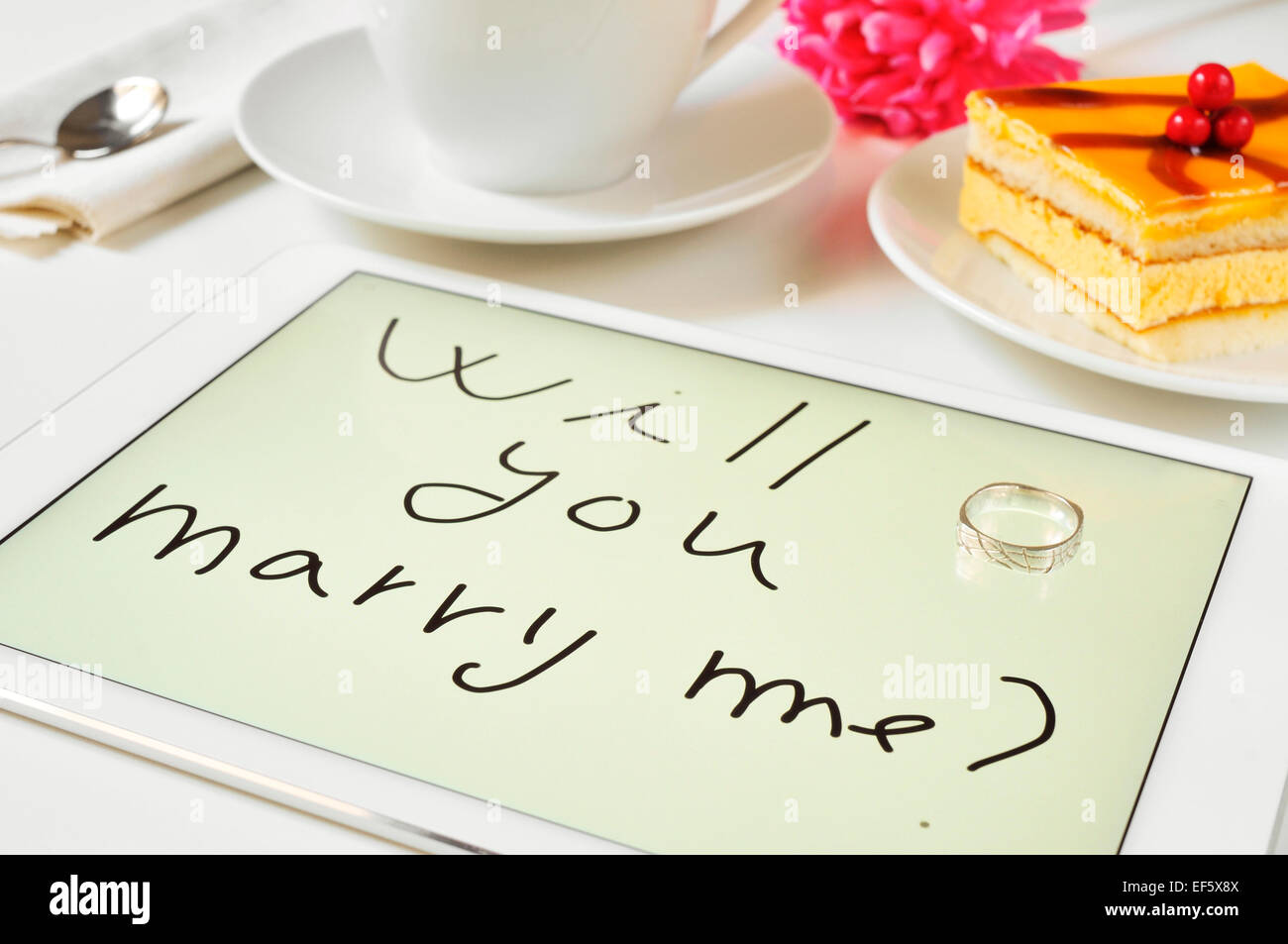 Un anello e la frase ti sposerà me? Scritto in una compressa su un tavolo al momento del dessert Foto Stock
