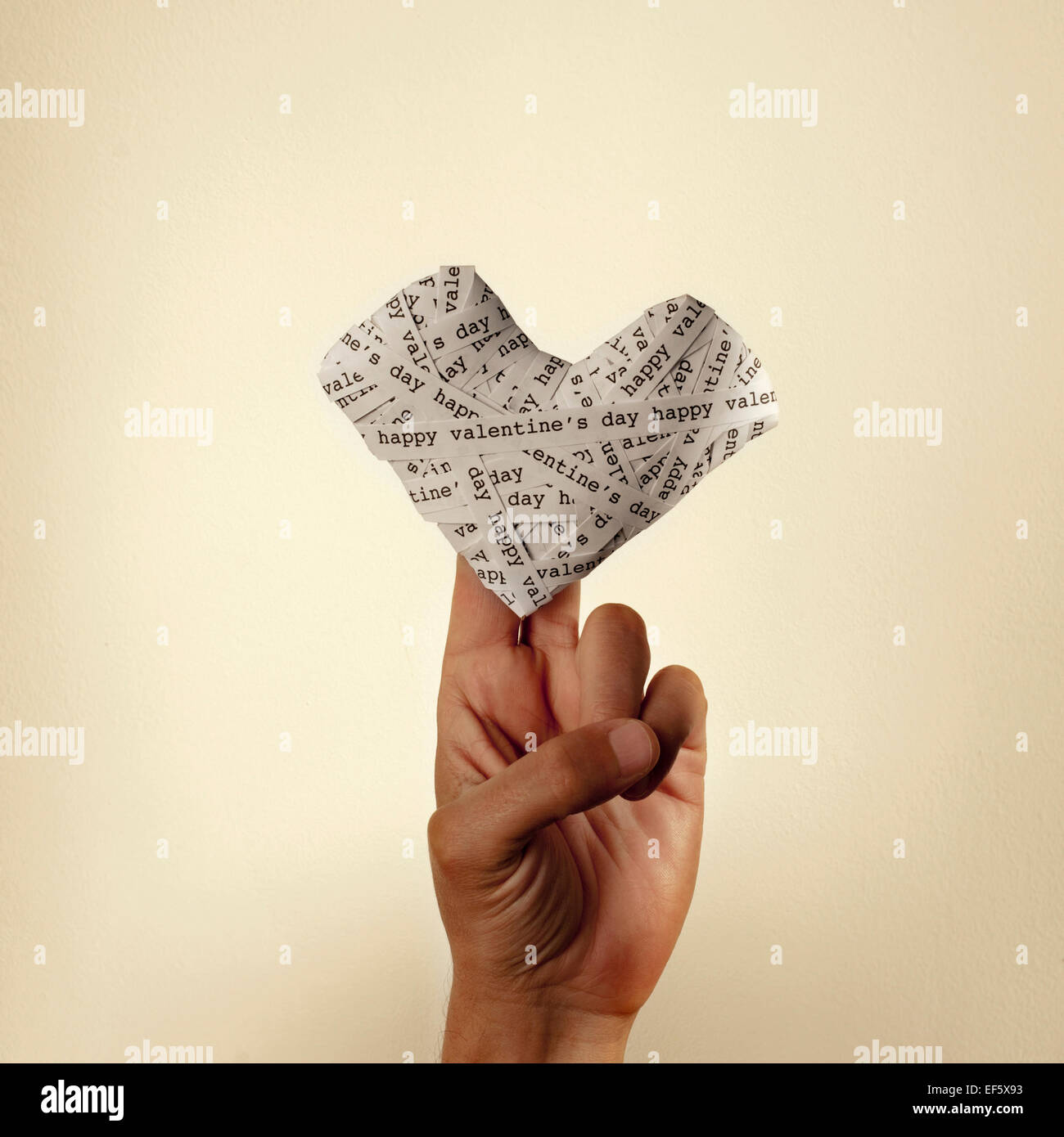La mano di un uomo giovane tenendo un cuore fatto con le strisce di carta con il testo felice il giorno di San Valentino, con un effetto retrò Foto Stock