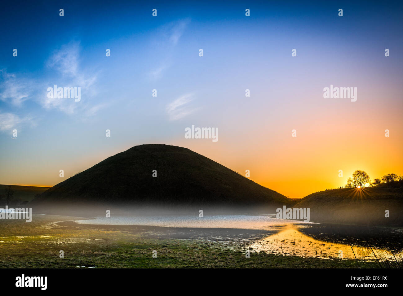 La nebbia si inclina come il sole sorge sopra il monumento storico di Silbury Hill nei pressi di Avebury nel Wiltshire. Foto Stock