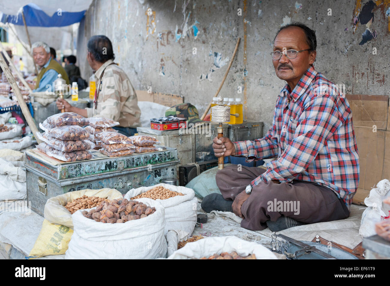 Leh, Ladakh, India. Il Bazaar Principale. Uomo con ruota di preghiera la vendita di frutta secca e noci Foto Stock