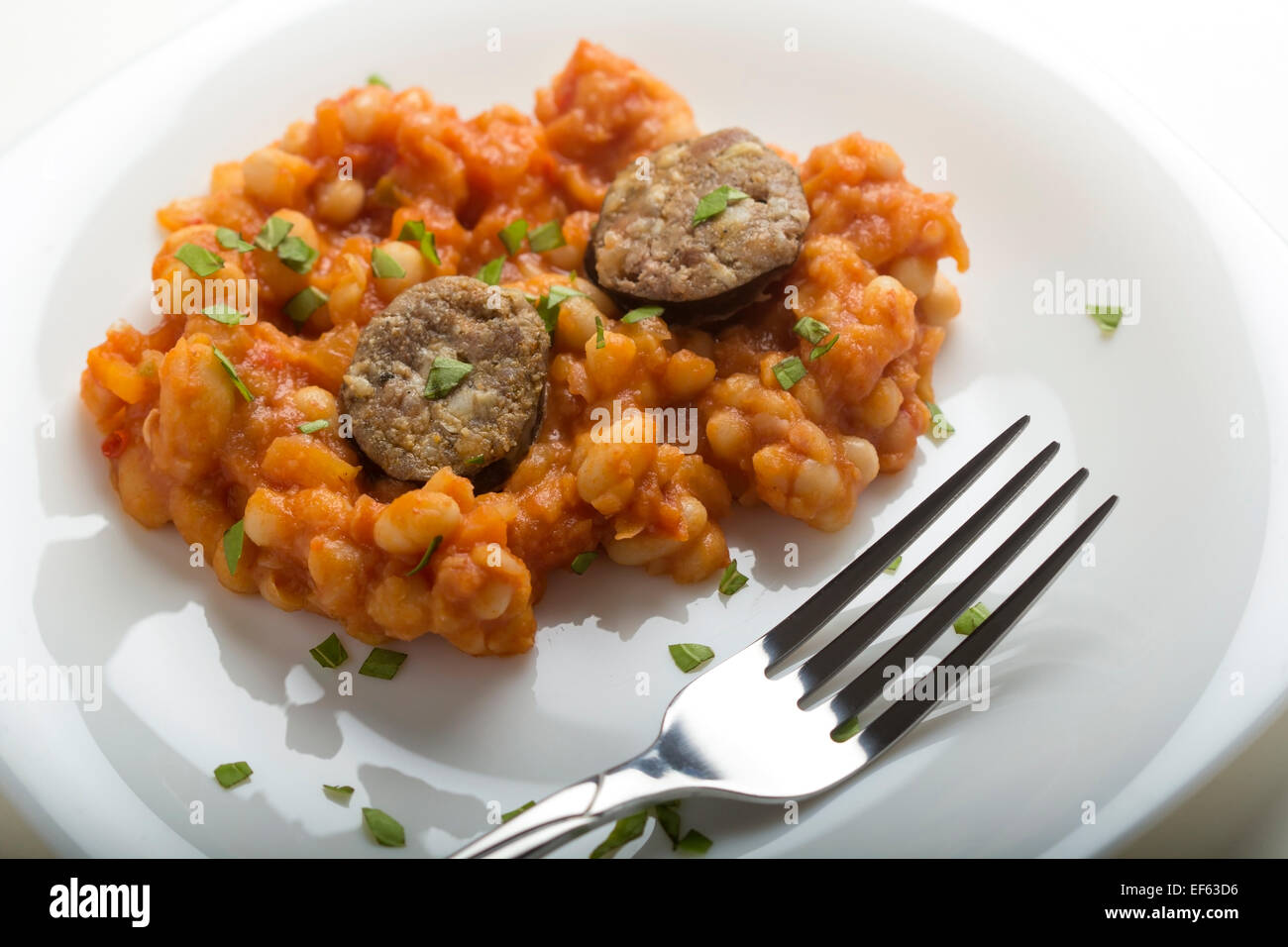 Salsicce di maiale con fagioli cotti sulla piastra bianca con forca Foto Stock