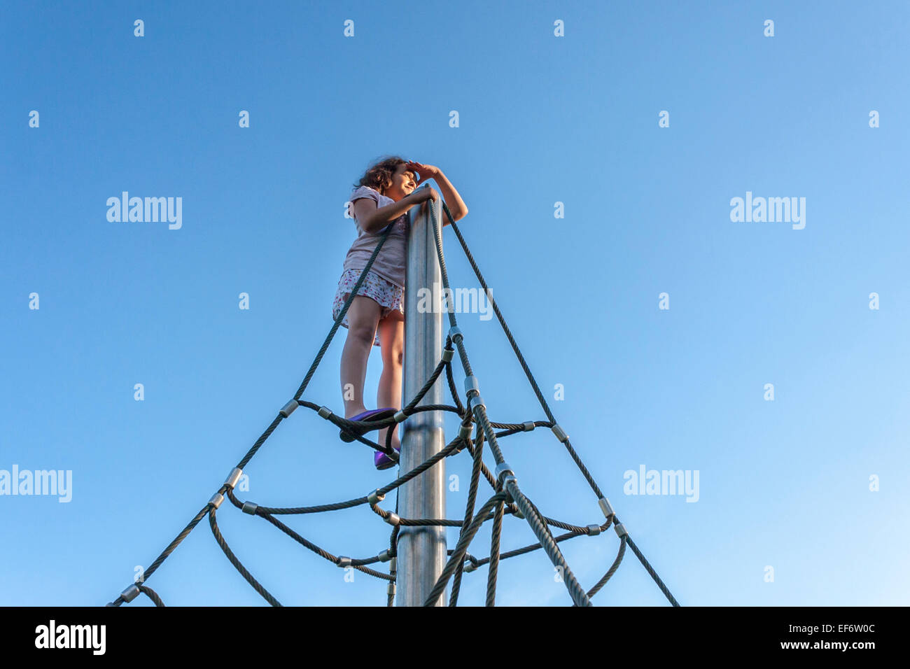 Fiducioso di nove anni vecchia ragazza sulla parte superiore di un telaio di arrampicata. Foto Stock